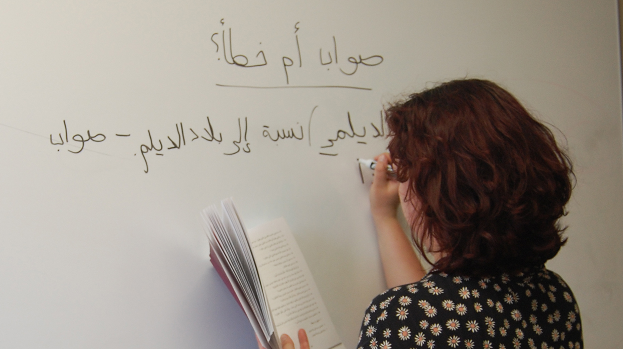 A woman uses a marker to write in Arabic on a whiteboard.