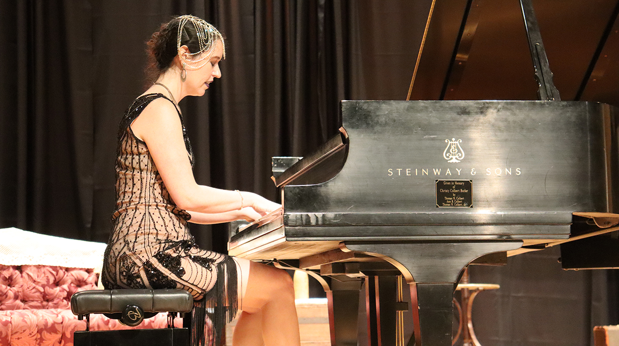 A woman wearing a black dress plays a piano on a stage.