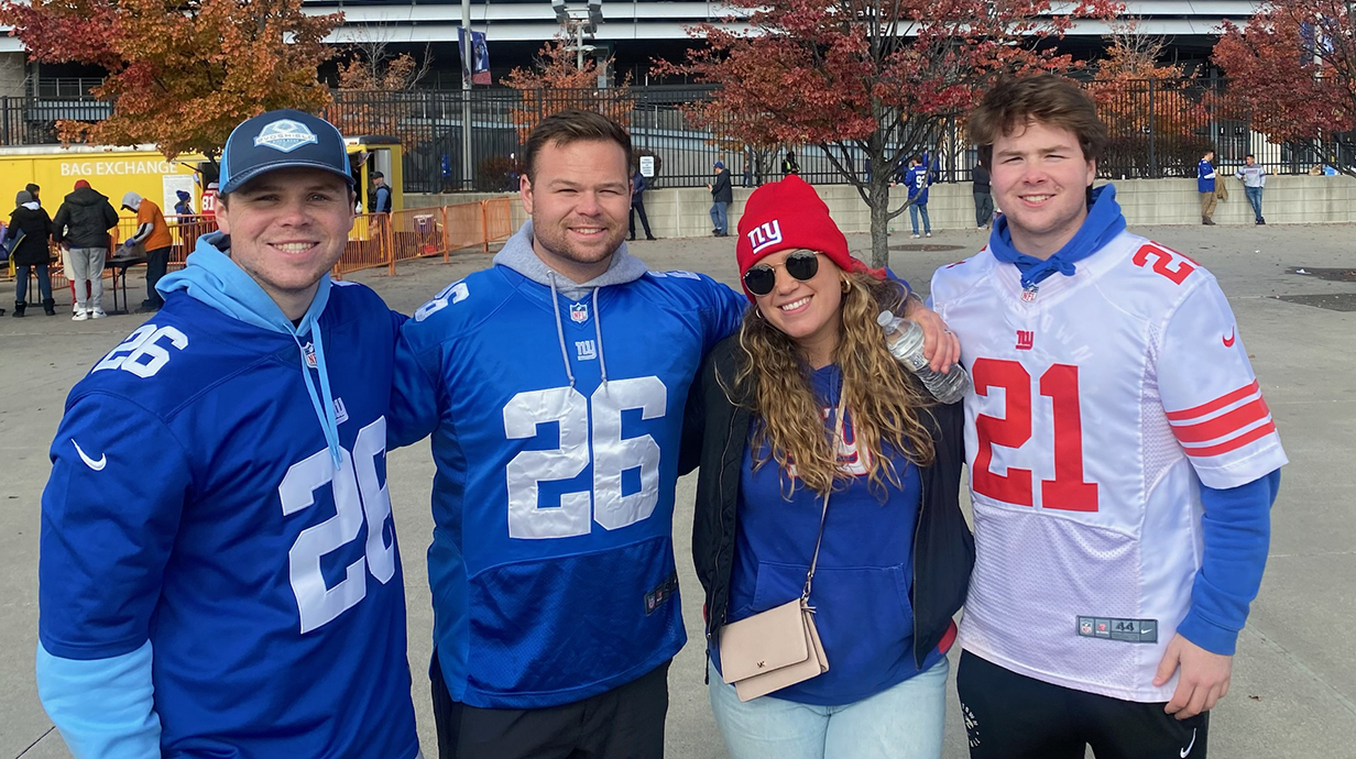 Four people wearing football jerseys stand outside a stadium.