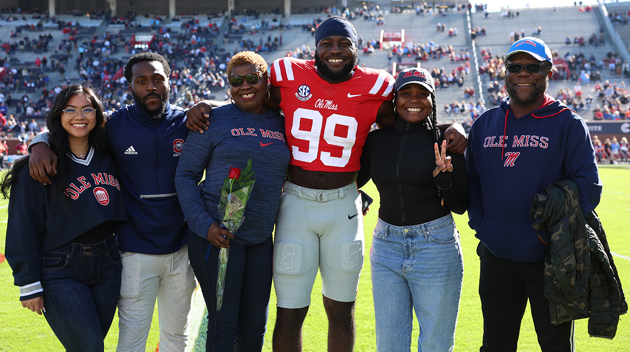 A football player and family members stand in a stadiium.