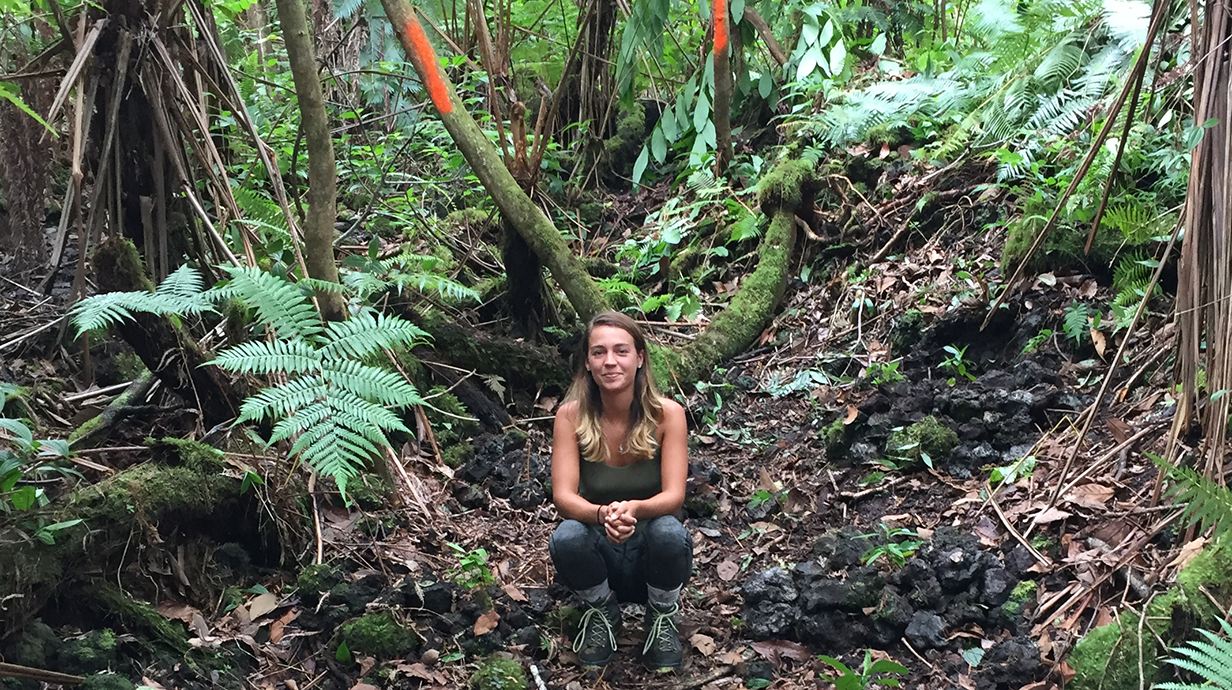 A woman squats on a trail in a jungle.