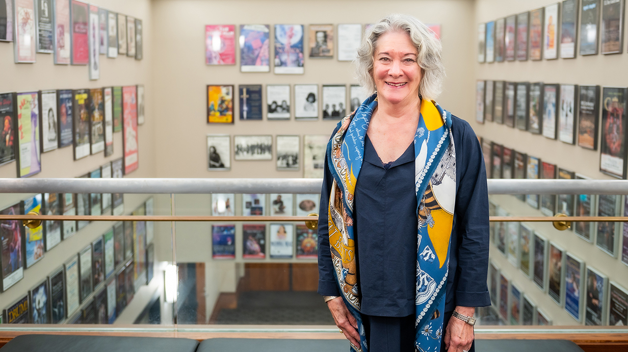 A woman stands on an elevated walkway with a large hall lines with theater posters behind her.