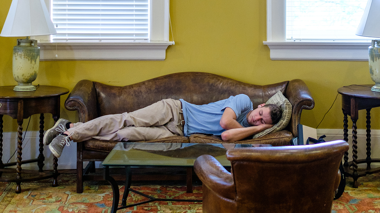A young man takes a nap on a sofa in a formal parlor.
