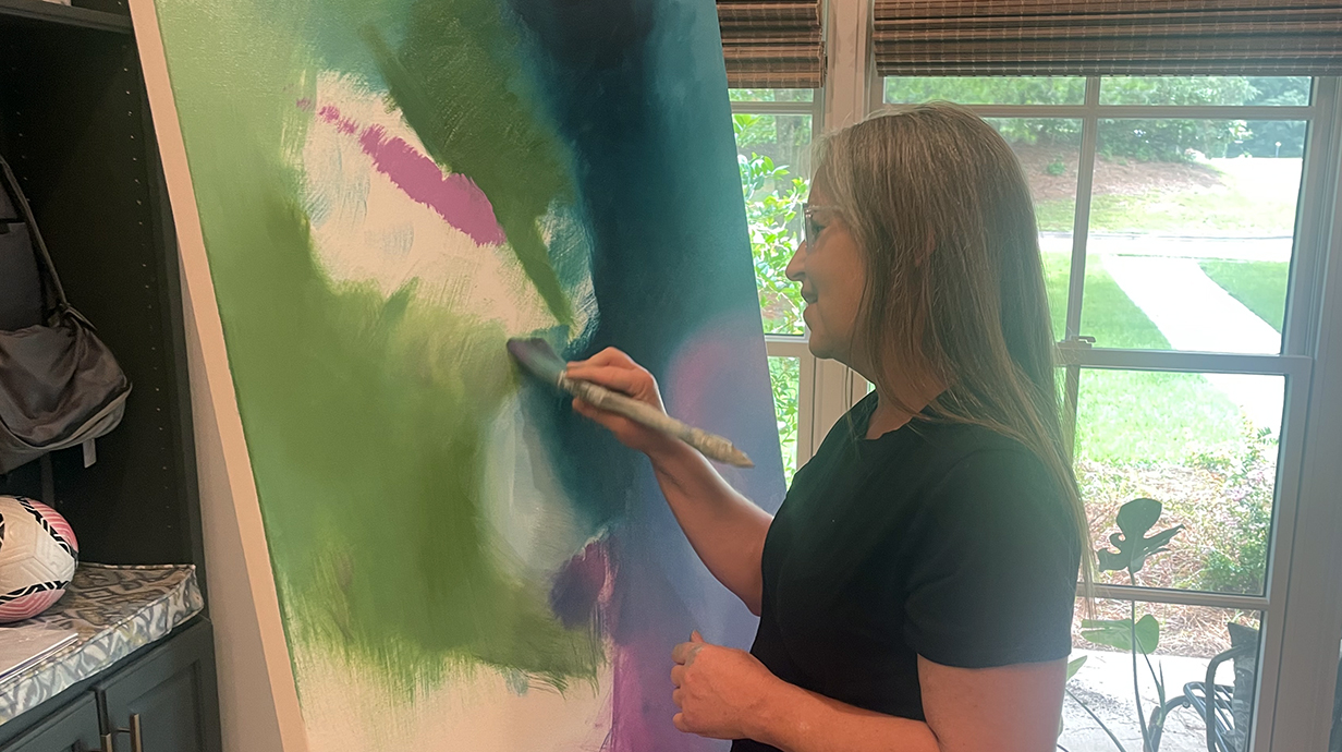 A woman paints on a large canvas in a home studio.