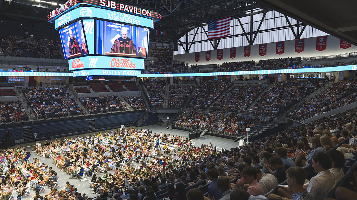 A speaker on a stage speaks to a crowded arena.