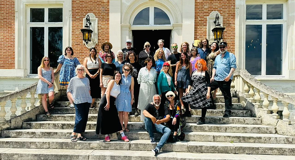 A large group of people pose for a photo on the front steps of an ornate red brick building.