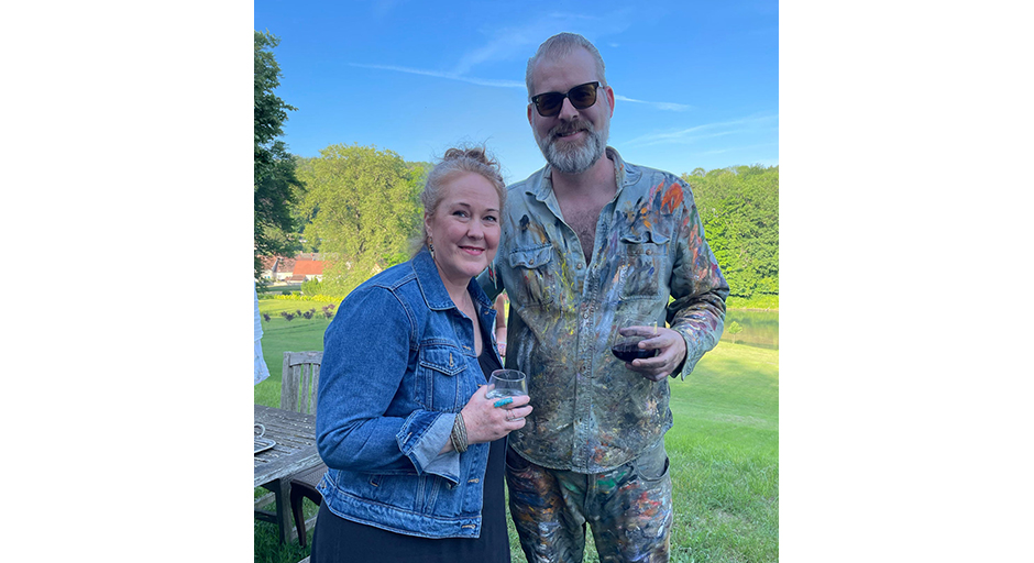 A woman and a man hold glasses of wine on a green lawn.