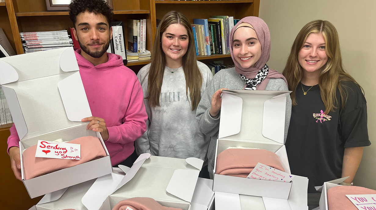 A young man and three young women look through pink and white promotional items for a public awareness campaign.