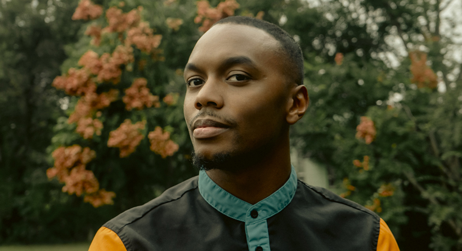 Portrait of a man standing outdoors in front of flowering shrubs.