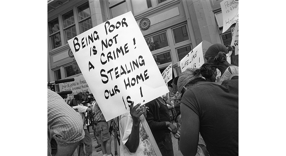 A protester holds a sign reading 'Being Poor Is Not a Crime!' at a rally.