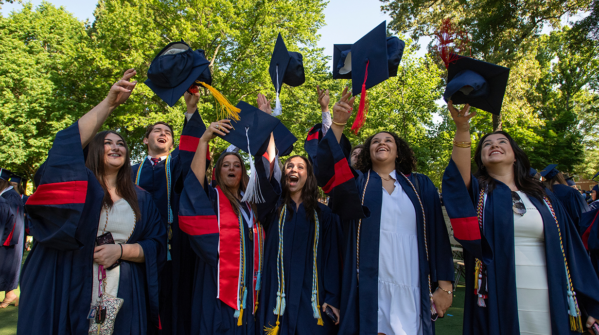 A group of young women wearing blue graduation robes toss their hats into the air.