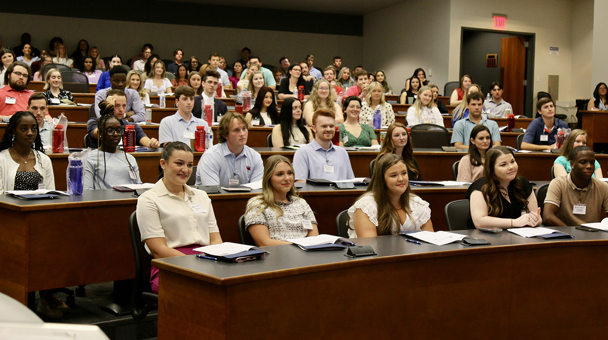 A large group of college students sits in an auditorium-style classroom.