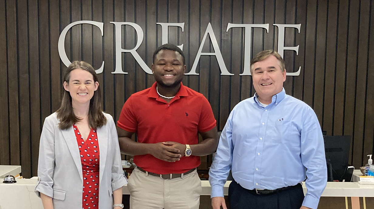 A woman and two men stand in a lobby in front of a wall sign reading 'CREATE Foundation.'