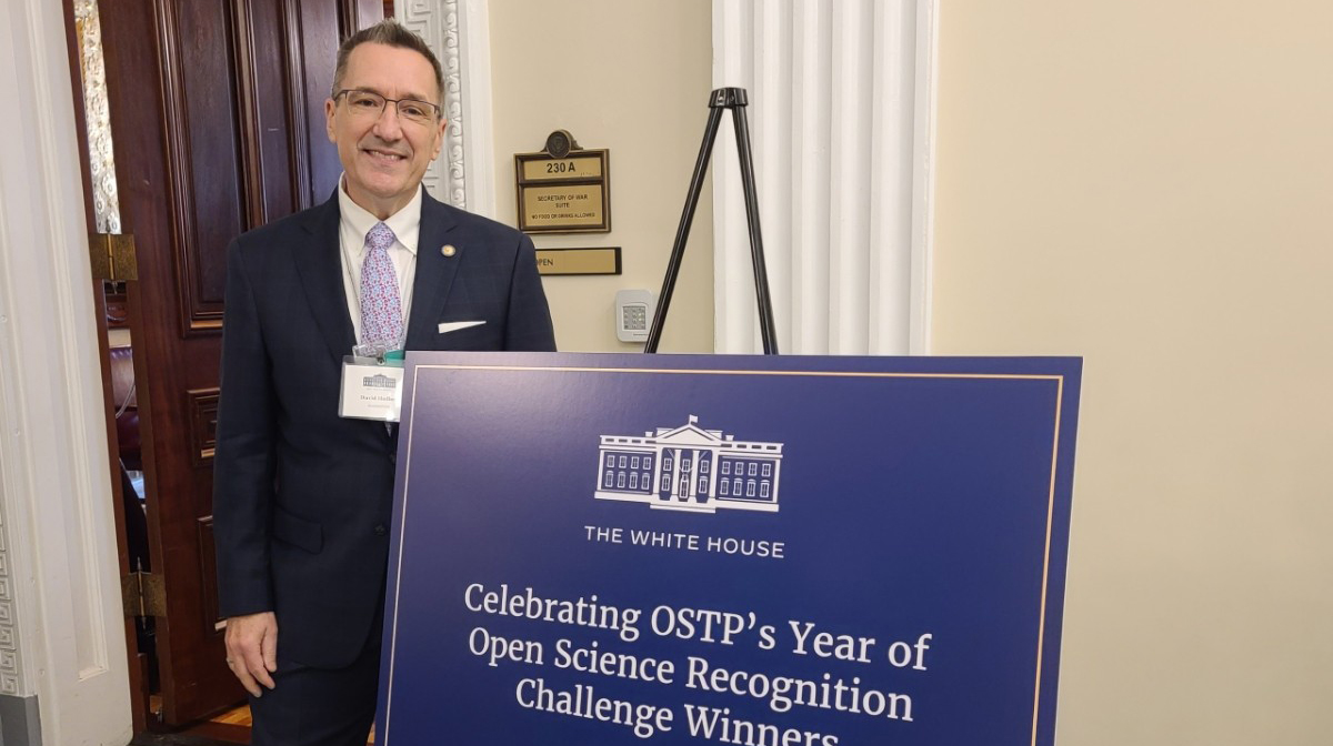 A man wearing a suit stands by a blue easel sign reading 'The White House: Celebrating OSTP's Year of Science Recognition Challenge Winners.'