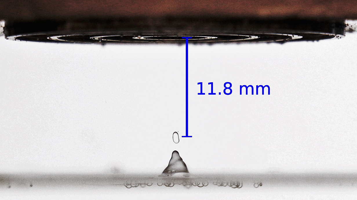 A sonic device pulls a droplet from the top of a container of water.