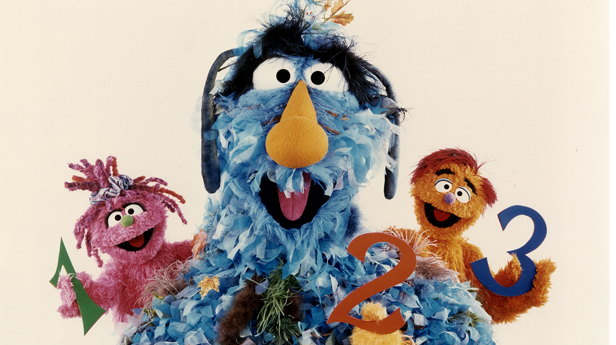 Three colorful, furry puppets smile and hold the numerals 1, 2 and 3.