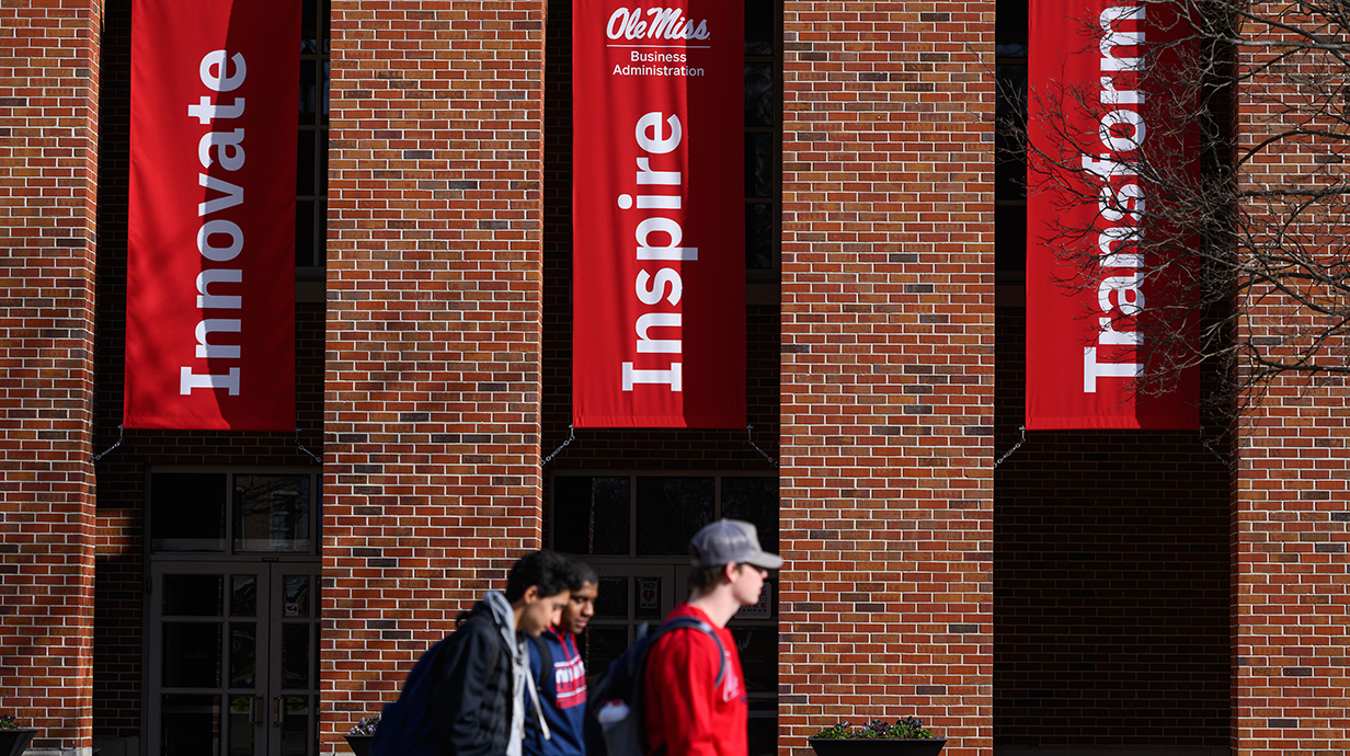 Three young men walk in front of a red brick building lined with red banners reading 'Innovate,' 'Inspire' and 'Transform.'