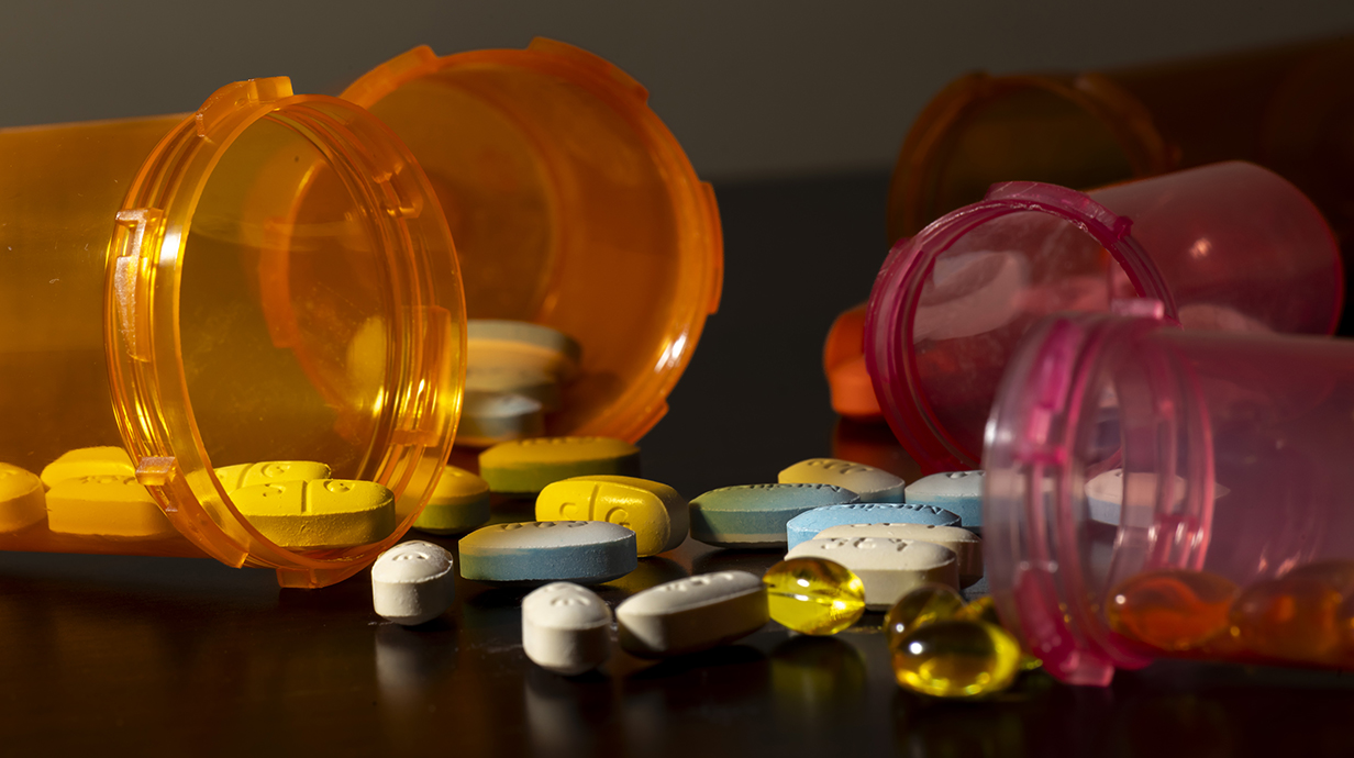 Several prescription pill bottles lie in a pile with pills spilling out of them.