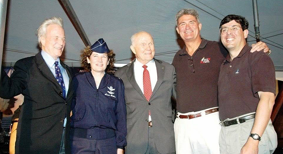 Four men and a woman in a military uniform gather underneath a giant tent.