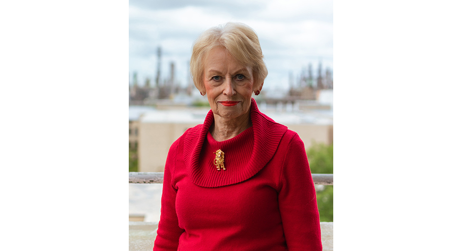 A woman wearing a red sweater stands in front of a refinery.