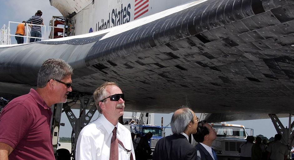 Two men inspect the underside of a space shuttle on a runway.