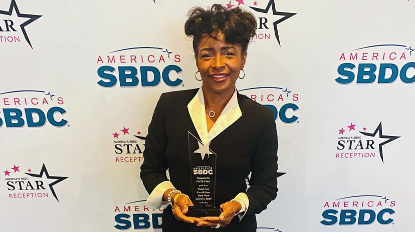 A woman stands in front of a printed backdrop holding a crystal award trophy.