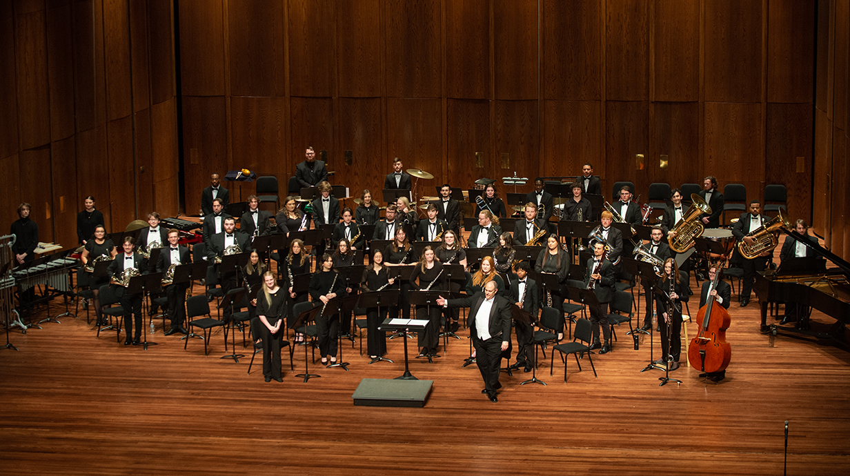 An orchestra stands onstage at the conclusion of a performance.