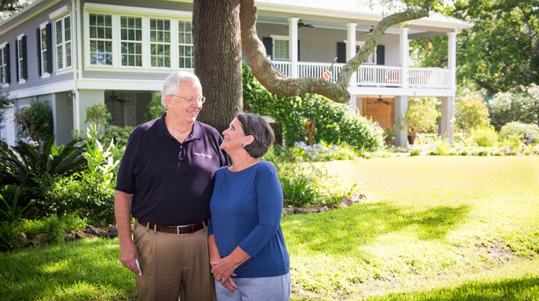 A man and woman stand outside a large house.