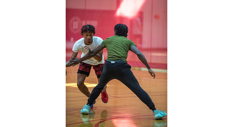 Two young men play basketball in a gym.