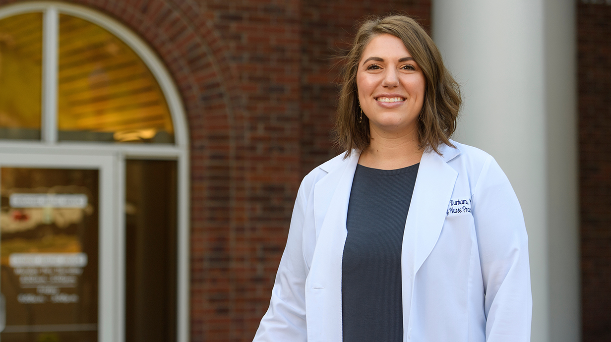 A woman in a doctor's white coat stands in front of a clinic.