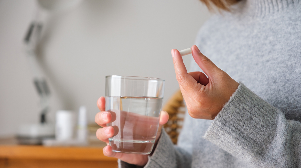 A woman holds a white pill and a glass of water.