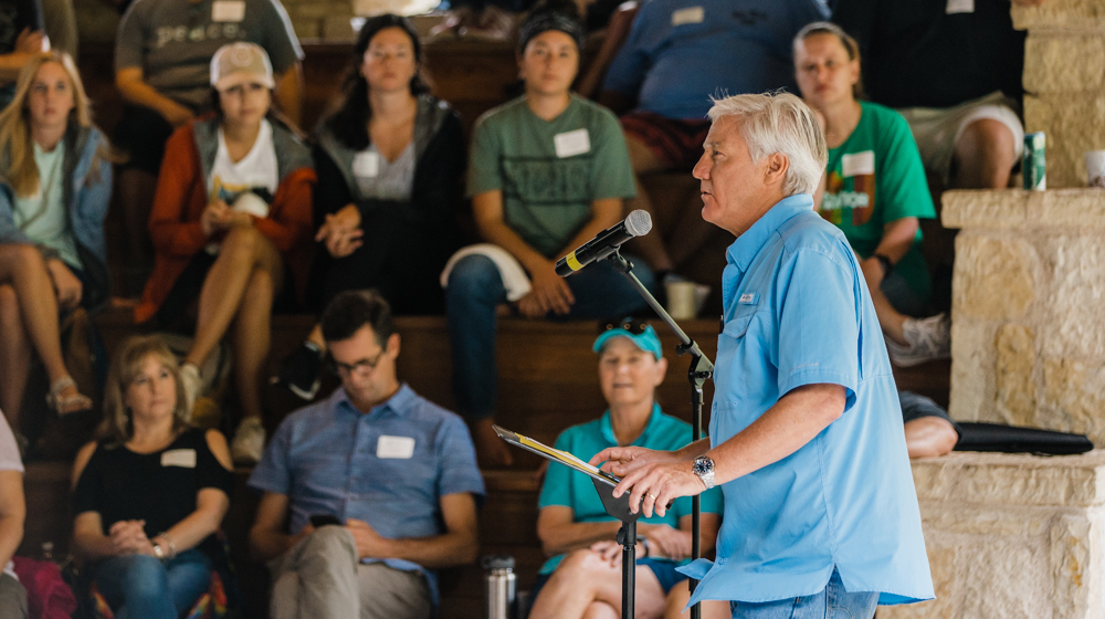 A man speaks to a large group of people in a tiered auditorium.