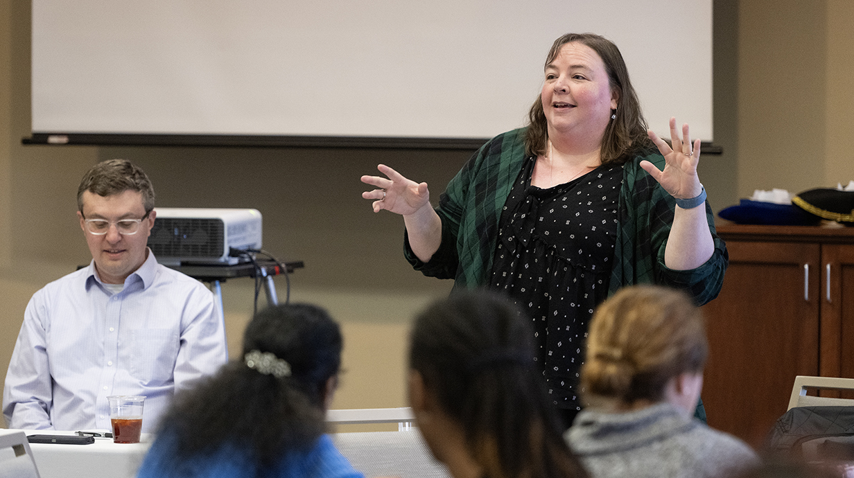 A woman talks and gestures to students from the front of a classroom.