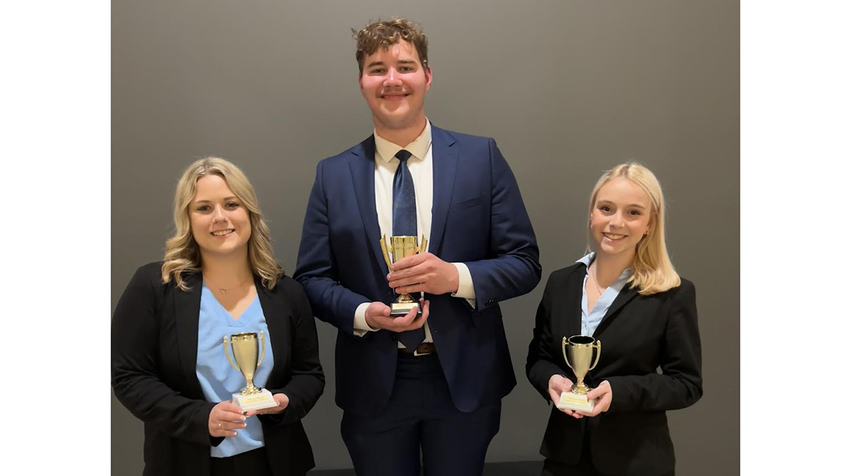 Two young women and a young man, all wearing business attire, show off award trophies.