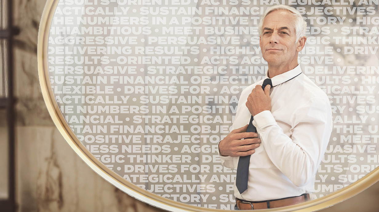 A silver-haired man standing in front of a screen lined with attributes of successful business leaders adjusts his tie.