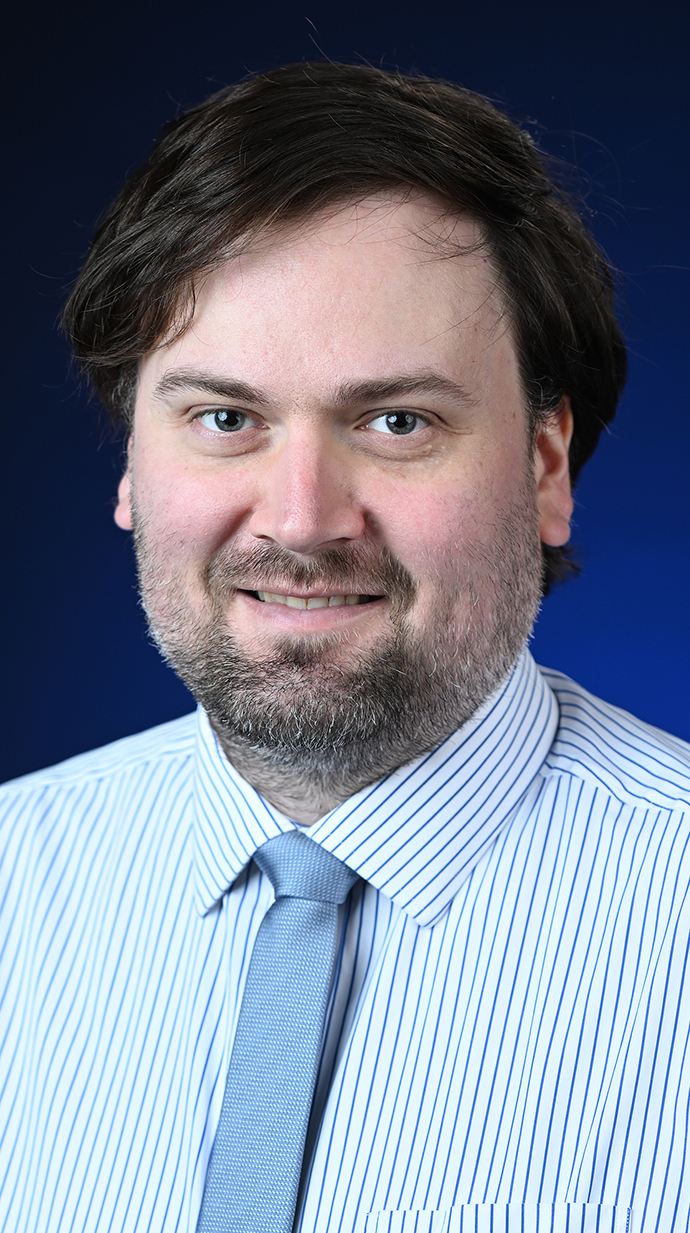 Headshot of a man wearing a blue and white striped shirt and a light blue tie.
