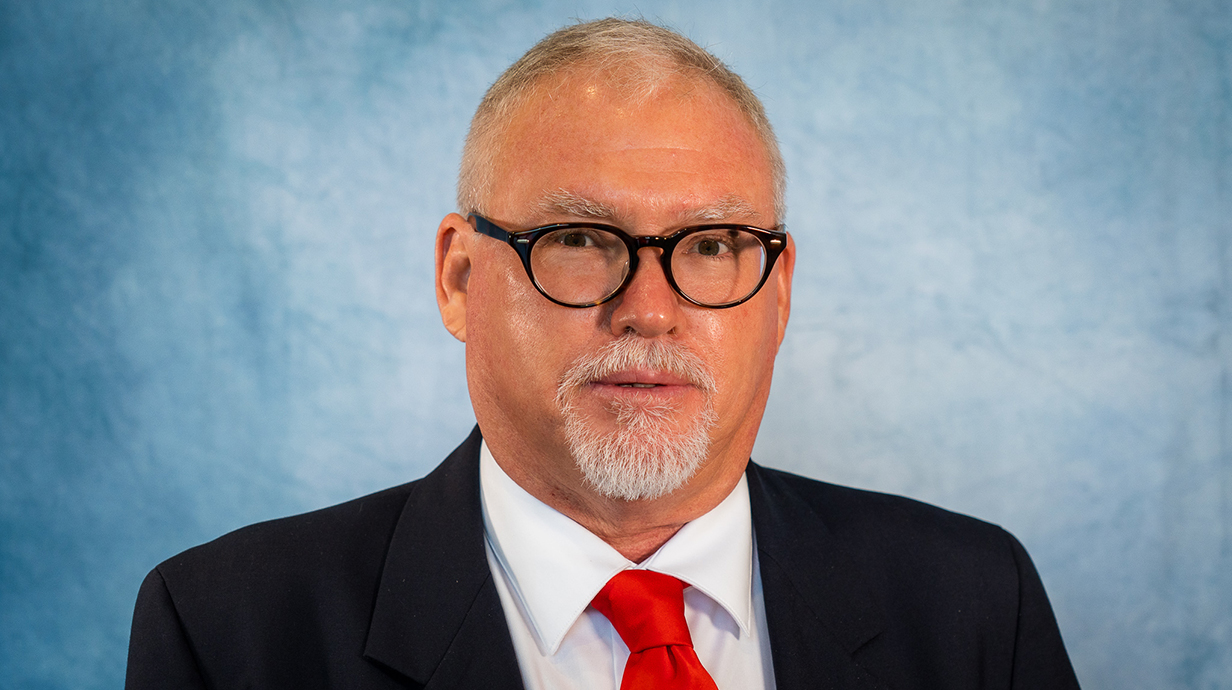 Portrait of a man wearing a dark blue suit against a light blue backdrop.