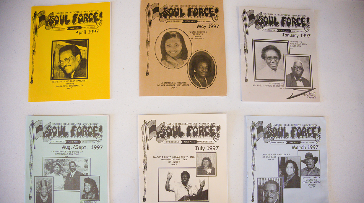 Artwork from several colorful newsletters hang on a wall.