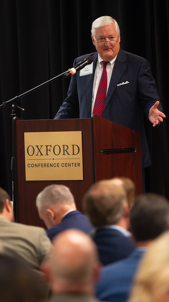 A man speaks from a podium in a crowded conference hall.