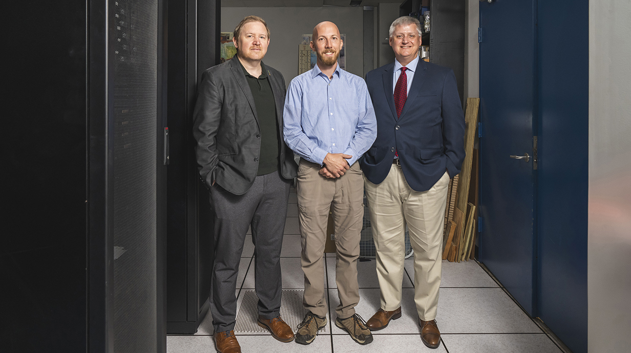 Three men stand between cabinets in a research space.