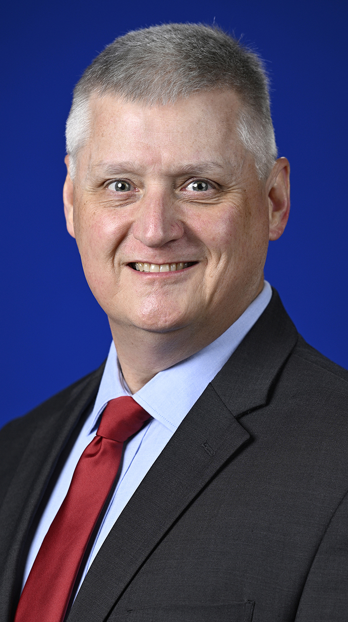 Headshot of a man wearing a dark suit and a red tie.