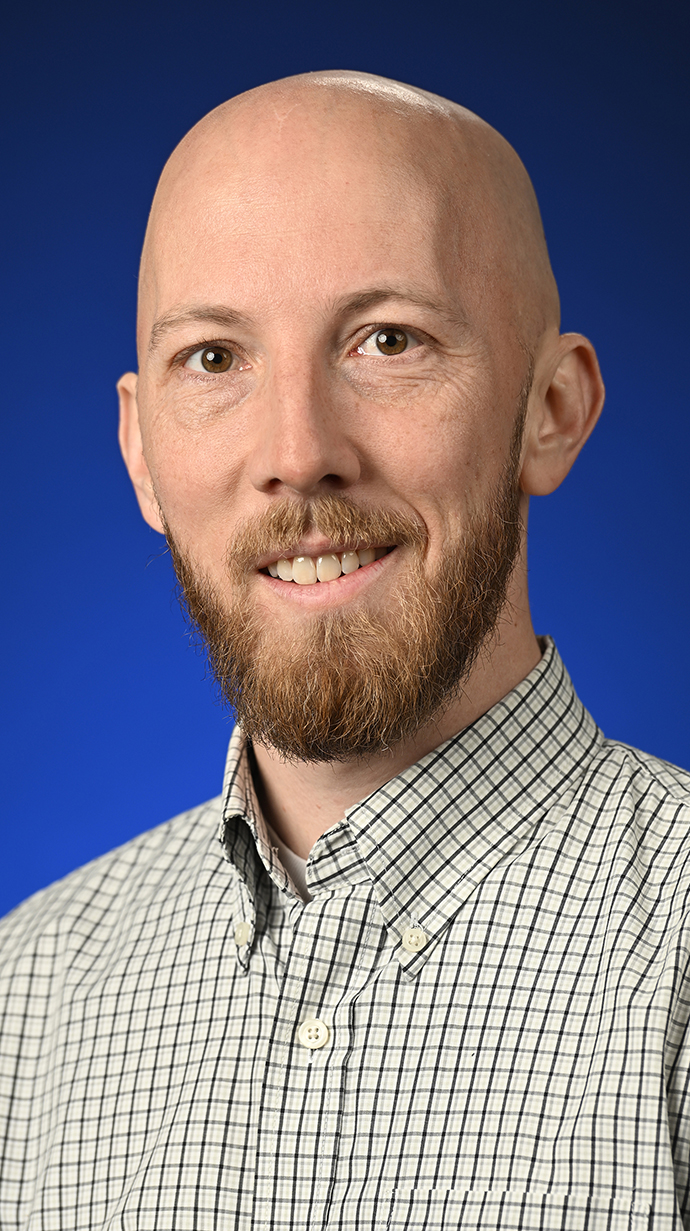 Headshot of a man wearing a brown and white patterned shirt.