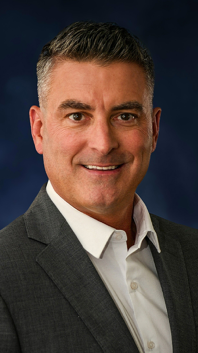 Headshot of a man wearing a gray jacket over a white shirt.