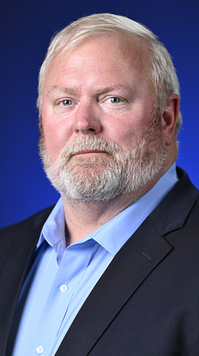 Headshot of a man wearing a dark jacket over a light blue shirt.