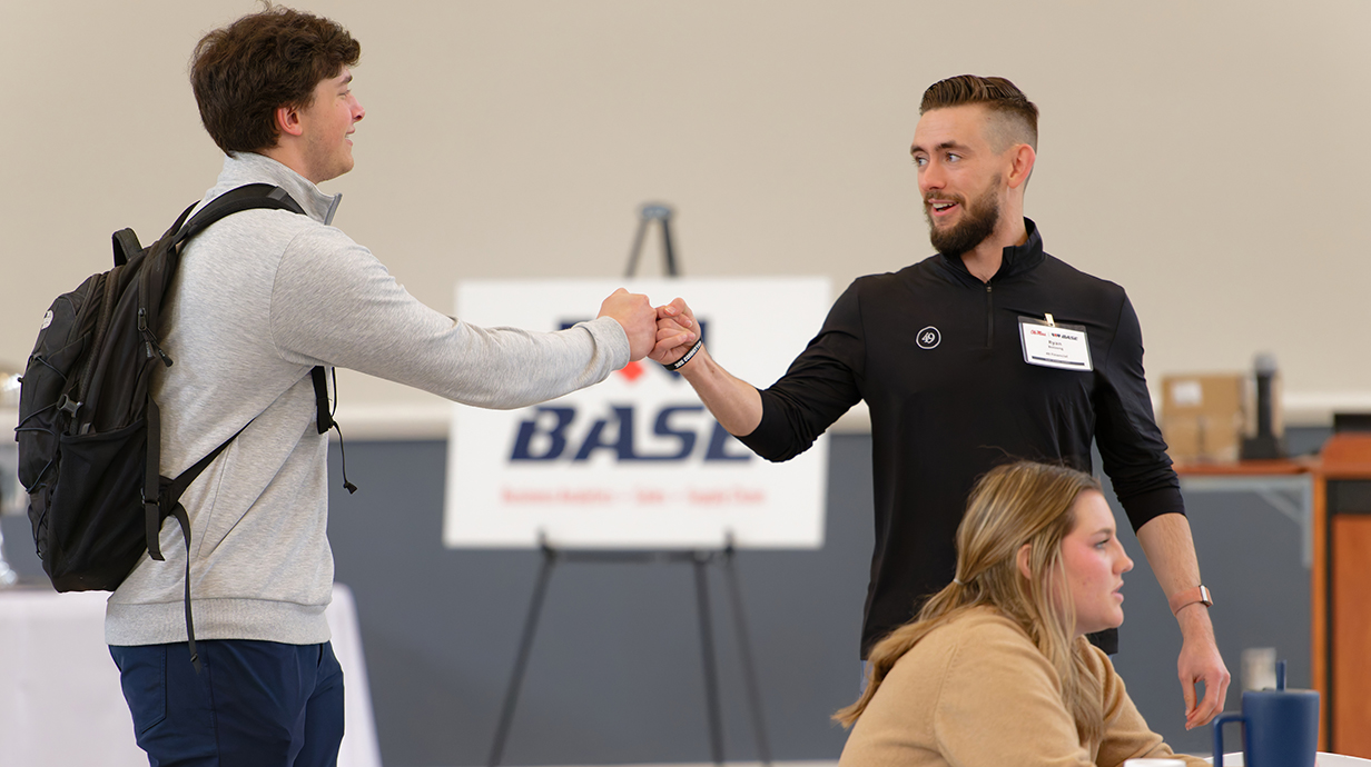 A man gives a young man a fist bump at the front of a conference hall.
