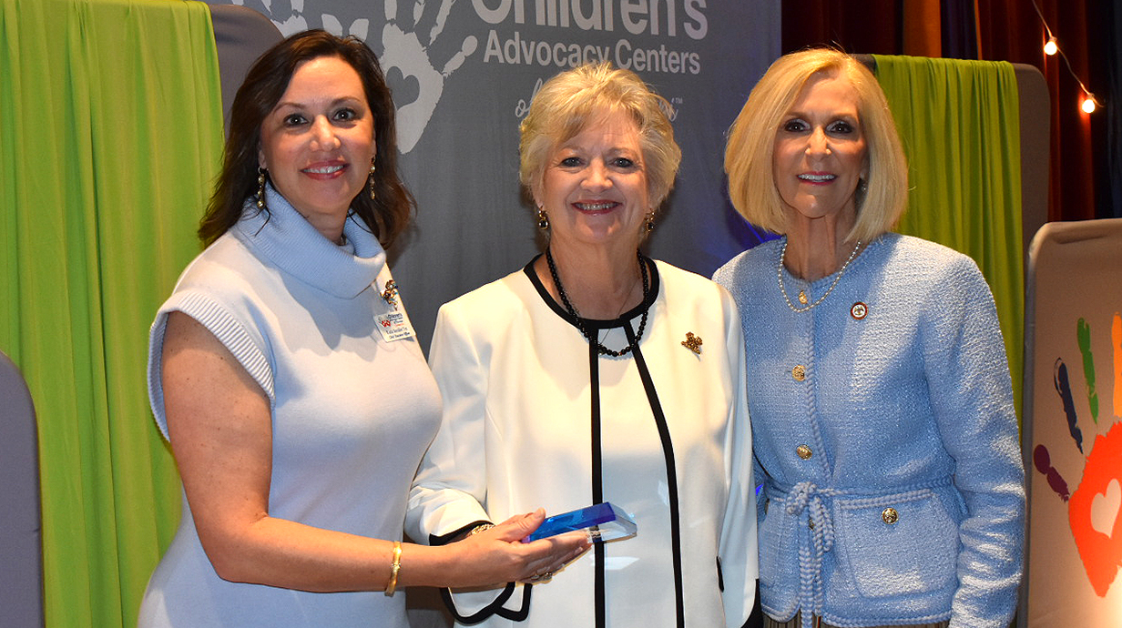 Two women present another woman with a crystal award trophy.