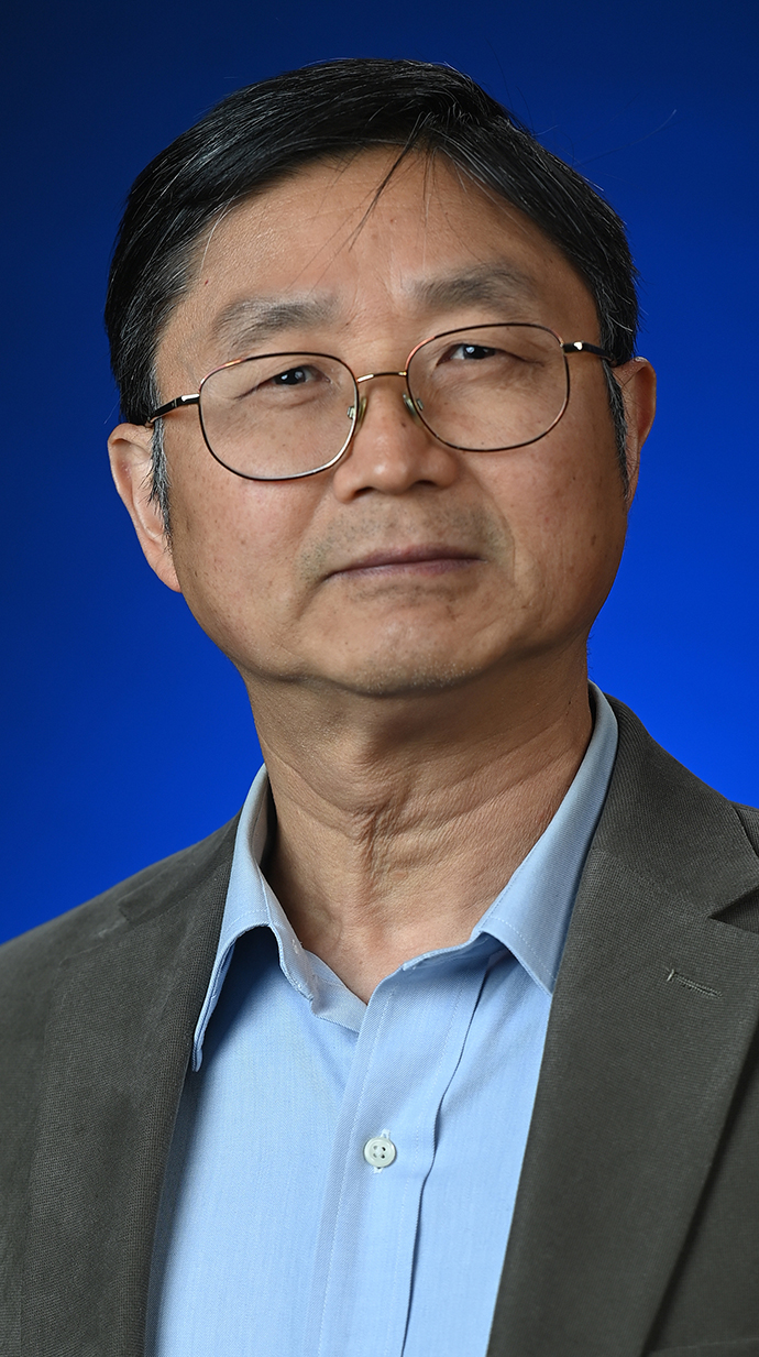 Headshot of a man wearing glasses and a gray jacket over a light blue shirt.