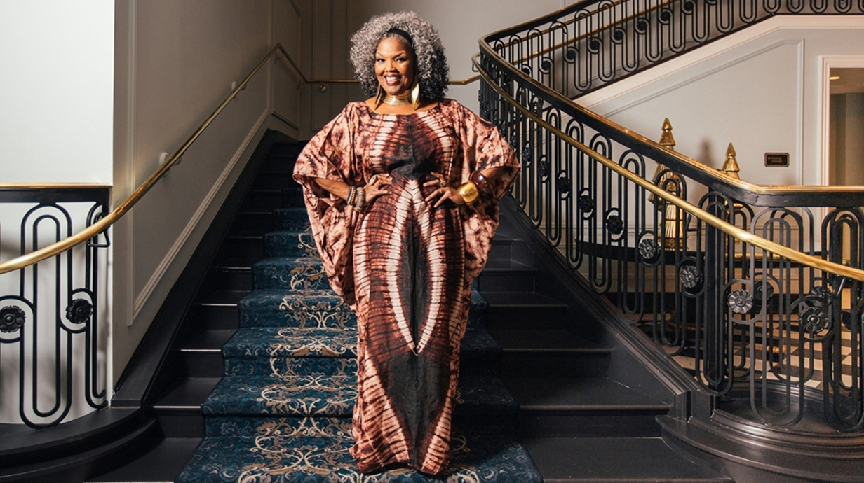A woman wearing an African-styled dress stands on an ornate staircase.