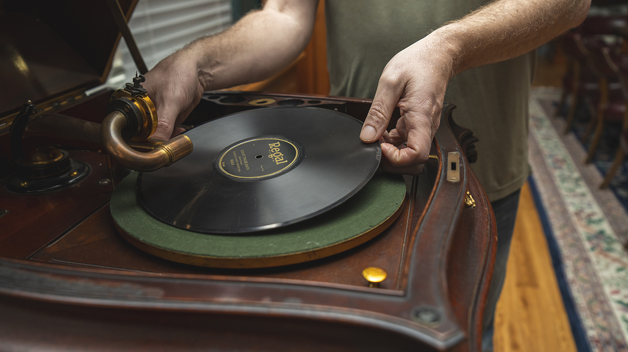 A hand places a vinyl record on a phonograph turntable.