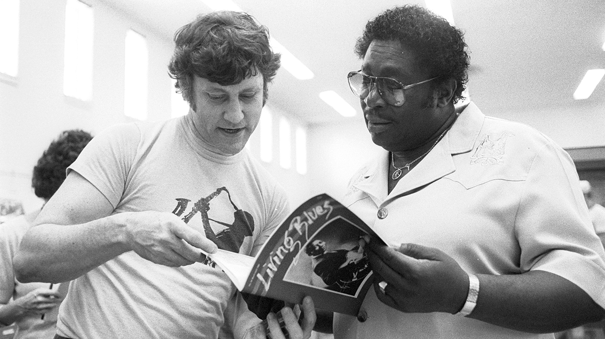 Black-and-white photograph of two men looking at a magazine.